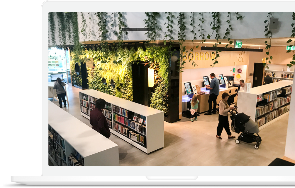 Una biblioteca bianca, moderna, con alle pareti piante e verde, popolata da persone che usufruiscono dei servizi digitali e innovativi, simbolo dell'attività di ISNG.